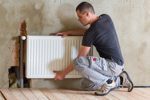 Un artisan installe un radiateur dans une maison en construction