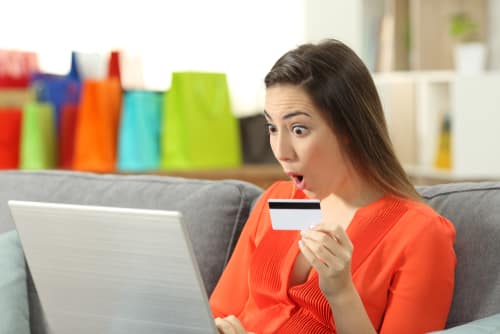 Une femme tient une carte bancaire et a une mauvaise surprise en ligne