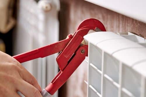 plombier Bayonne - Un artisan répare un radiateur à l'aide d'une clé de serrage.