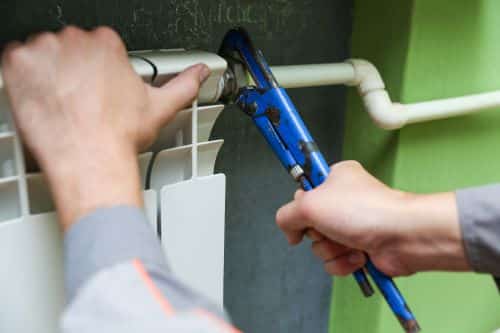 Plombier Cagnes-sur-Mer - Un artisan plombier répare un radiateur avec un outil.