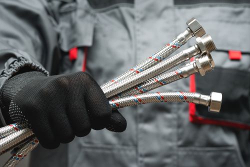 Plombier Niort : Un plombier tient dans sa main plusieurs tuyaux flexibles.