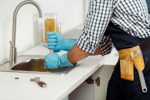 Plombier Saint-Quentin - Un plombier en train de déboucher un évier de cuisine.