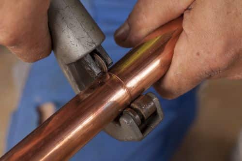 plombier Livry-Gargan - un plombier découpe un tuyau de cuivre
