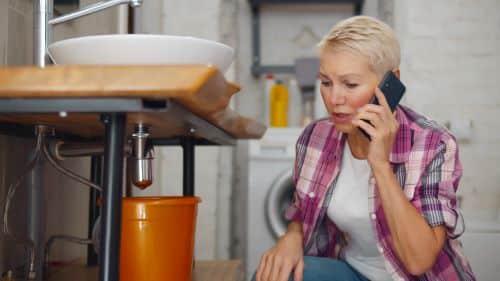 plombier montpellier - une femme constate une fuite sous son lavabo