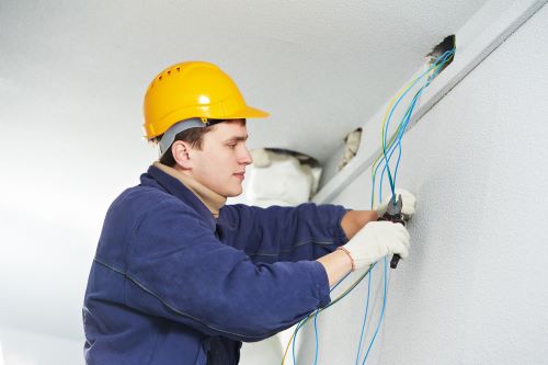 Électricien Angers - Un électricien coupe des câbles électriques au plafond.