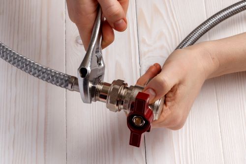 Plombier Castres - Un plombier fait le raccordement de deux tuyaux flexibles en acier inoxydable.