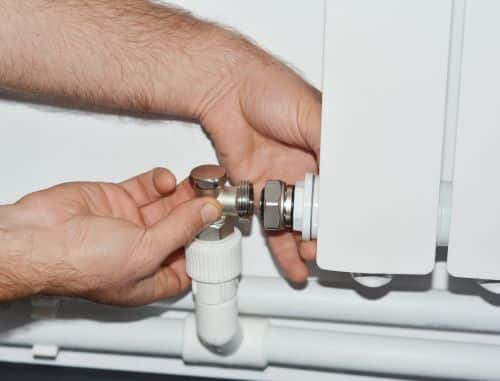 Plombier Istres - Un plombier raccorde les tuyaux d'eau d'un radiateur.
