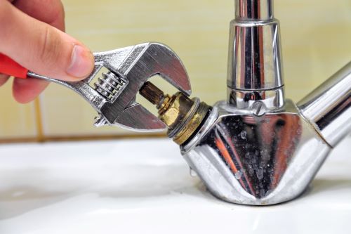 Plombier Saint-Priest - Un plombier répare un robinet avec une clé à molette.
