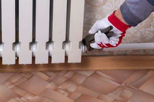 Plombier Thionville - Un plombier raccorde un radiateur en fonte au système de chauffage d'une maison.