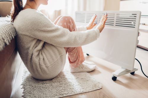 Chauffagiste Annecy - Une femme se réchauffe auprès d'un radiateur.