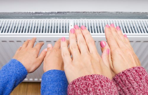 Chauffagiste Évreux - Une femme et un enfant se réchauffent les mains auprès d'un radiateur.