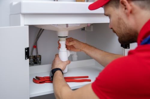 Plombier Tressin - Un artisan installe un siphon dans une salle de bains.