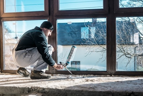 Vitrier Vénissieux - Un artisan vitrier répare une baie vitrée en utilisant de la mousse polyuréthane.