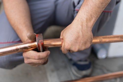 plombier Vienne - un plombier chauffagiste découpe un tuyau en cuivre