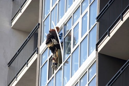 vitrier Lunel - Un vitrier suspendu sur la façade d'un immeuble, installe des fenêtres.