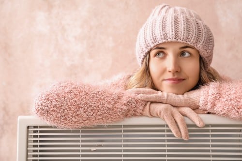 Chauffagiste Herblay - Une femme se réchauffe près de son radiateur