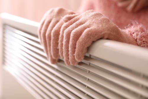 chauffagiste Auch - Une femme se réchauffe les mains sur un radiateur