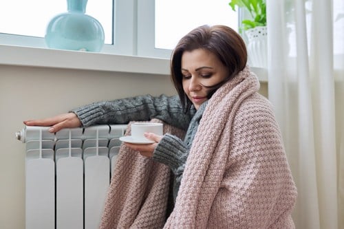 chauffagiste Aurillac - Une femme se réchauffe près de son radiateur