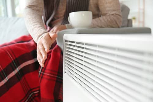 chauffagiste Dax - Une femme se réchauffe les mains sur un radiateur