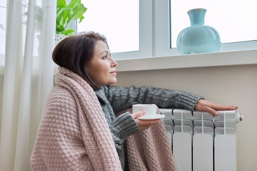 chauffagiste Elancourt - Une femme se réchauffe près de son radiateur