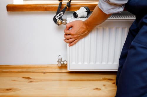 chauffagiste Les Mureaux - Un plombier chauffagiste qui répare un radiateur