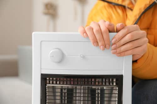 chauffagiste Lisieux - Une femme se réchauffe les mains près de son radiateur électrique