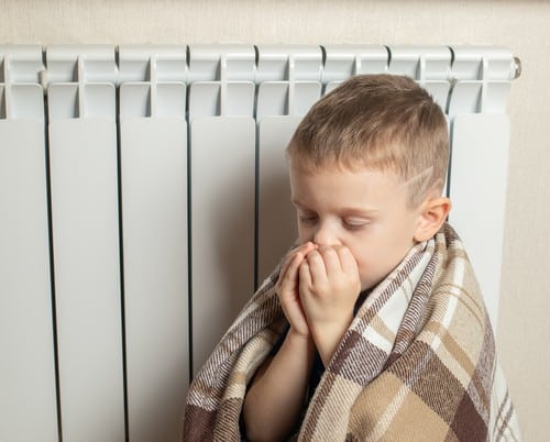 chauffagiste Nevers - Un enfant se réchauffe à côté d'un radiateur