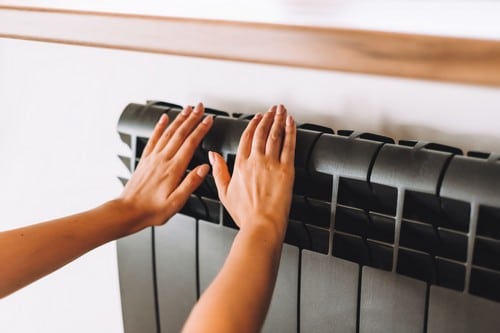 chauffagiste Orange - Une femme se chauffe les mains sur un radiateur.