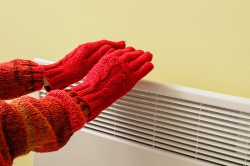 chauffagiste Pontoise - Une femme se réchauffe les mains près d'un radiateur