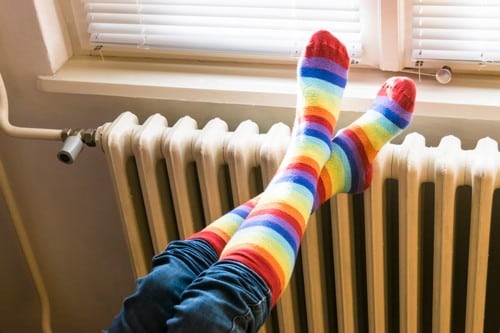chauffagiste Romans-sur-Isère - Une femme se réchauffe les pieds sur un radiateur.