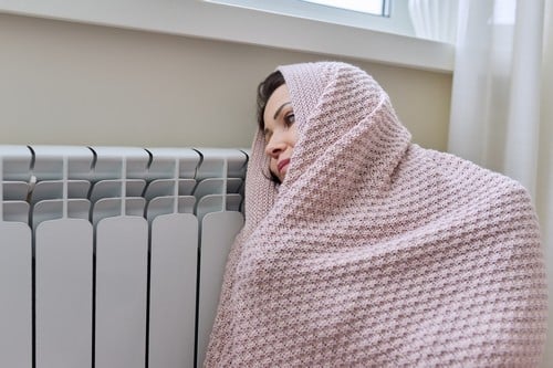 chauffagiste Vanves - Une femme se réchauffe près de son radiateur