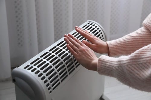 chauffagiste Vierzon - Une femme se rréchauffe les mains devant un radiateur