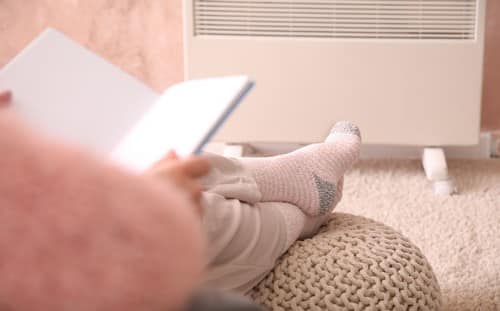 chauffagiste Melun - Une femme lit une livre les pieds au chaud devant le radiateur