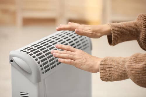chauffagiste Arcueil - Une femme se réchauffe les mains près de son radiateur