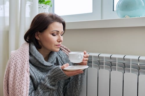 chauffagiste Nogent-sur-Oise - une femme se réchauffe à côté d'un radiateur