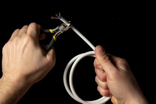 Électricien Lyon 2 - les bons artisans - mains qui tiennent une pince et un fil électrique