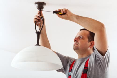 Electricien Quinsac - homme qui installe une lampe au plafond