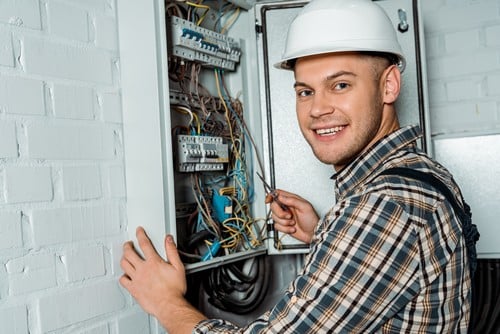 Electricien Villennes-sur-Seine - homme qui sourit devant un tableau électrique
