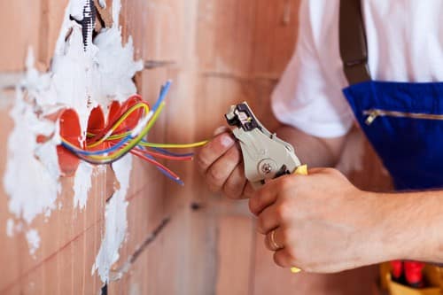 Electricien Paris 12 - mains d'un homme qui règlent les câbles électriques dans un mur