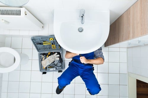 Plombier Amboise - homme qui règle la tuyauterie d'un lavabo