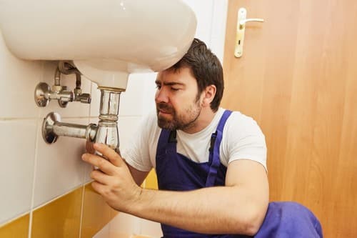 Plombier Morangis - homme qui règle une tuyauterie sous un évier