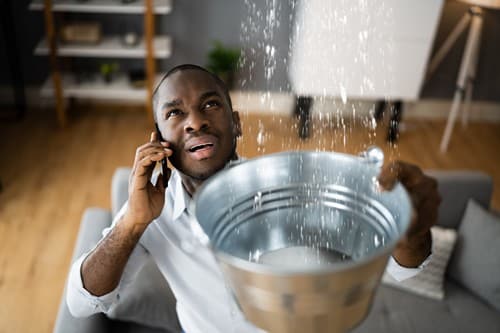 Plombier Verneuil-sur-Seine - homme au téléphone qui tient un seau d'eau car fuite d'eau