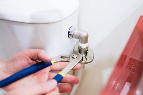 Plombier Lucé - mains d'un homme qui règle un tuyau du cabinet toilette