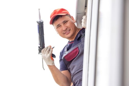 Vitrier Capinghem - homme qui sourit par la fenêtre en tenant un outil pour installer une fenêtre