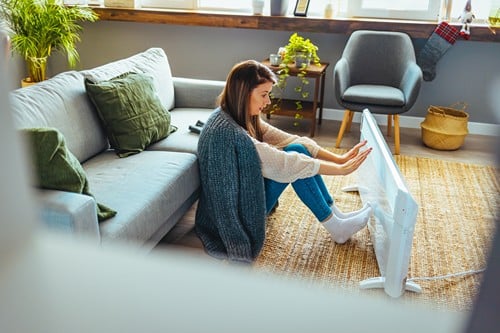 Chauffagiste Bischwiller - les bons artisans - dame qui se réchauffe contre un radiateur électrique