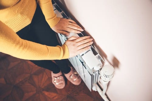 Chauffagiste Sin-le-Noble - femme qui pose les mains sur le chauffage pour se réchauffer