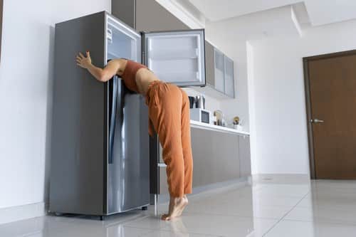 Climatisation Poissy - les bons artisans - femme qui à chaud et qui met la tête dans son frigo