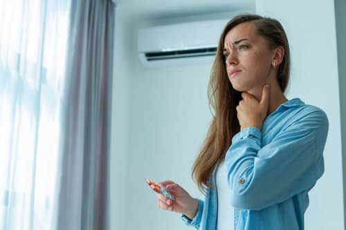 climatisation Bobigny - une femme se tient la gorge en tenant la télécommande d'une climatisation