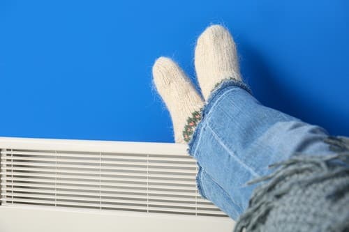 une personne pose ses pieds sur un radiateur à inertie