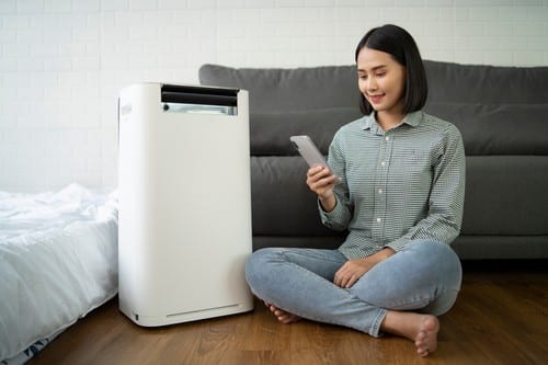 Climatisation Gif-sur-Yvette - femme qui se tient devant un climatiseur en tenant une télécommande